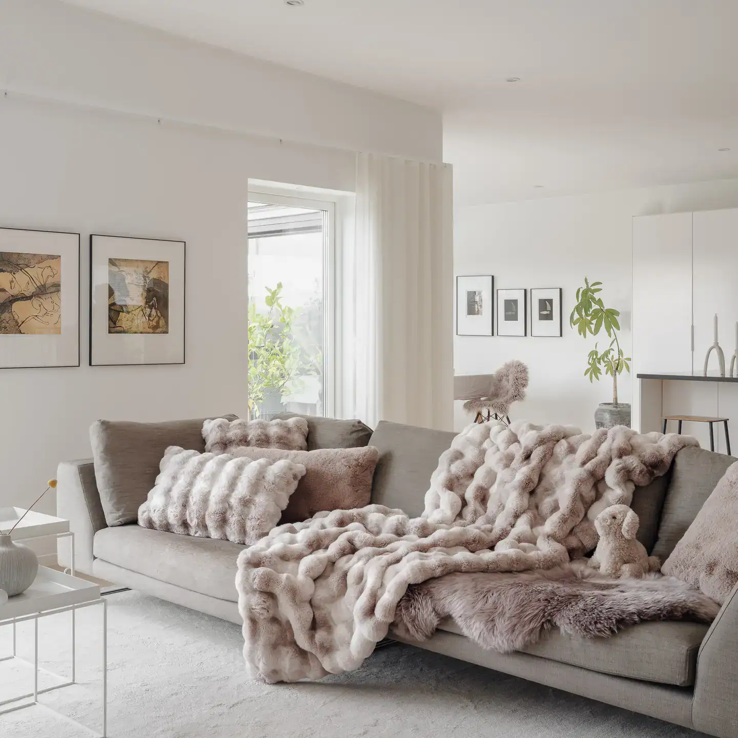 Divano bianco elegante con coperte in pelliccia sintetica e decorazioni moderne.