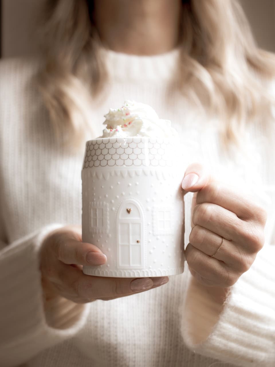 Un tazza bianca decorata con dettagli eleganti, tenuta da una donna con maglione bianco, ambiente lu.