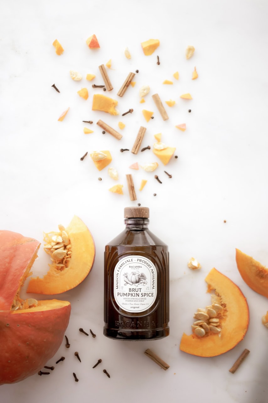 Aggiunta di spezie di zucca fresca in un flacone di vetro con pezzi di zucca e spezie sparsi intorno.