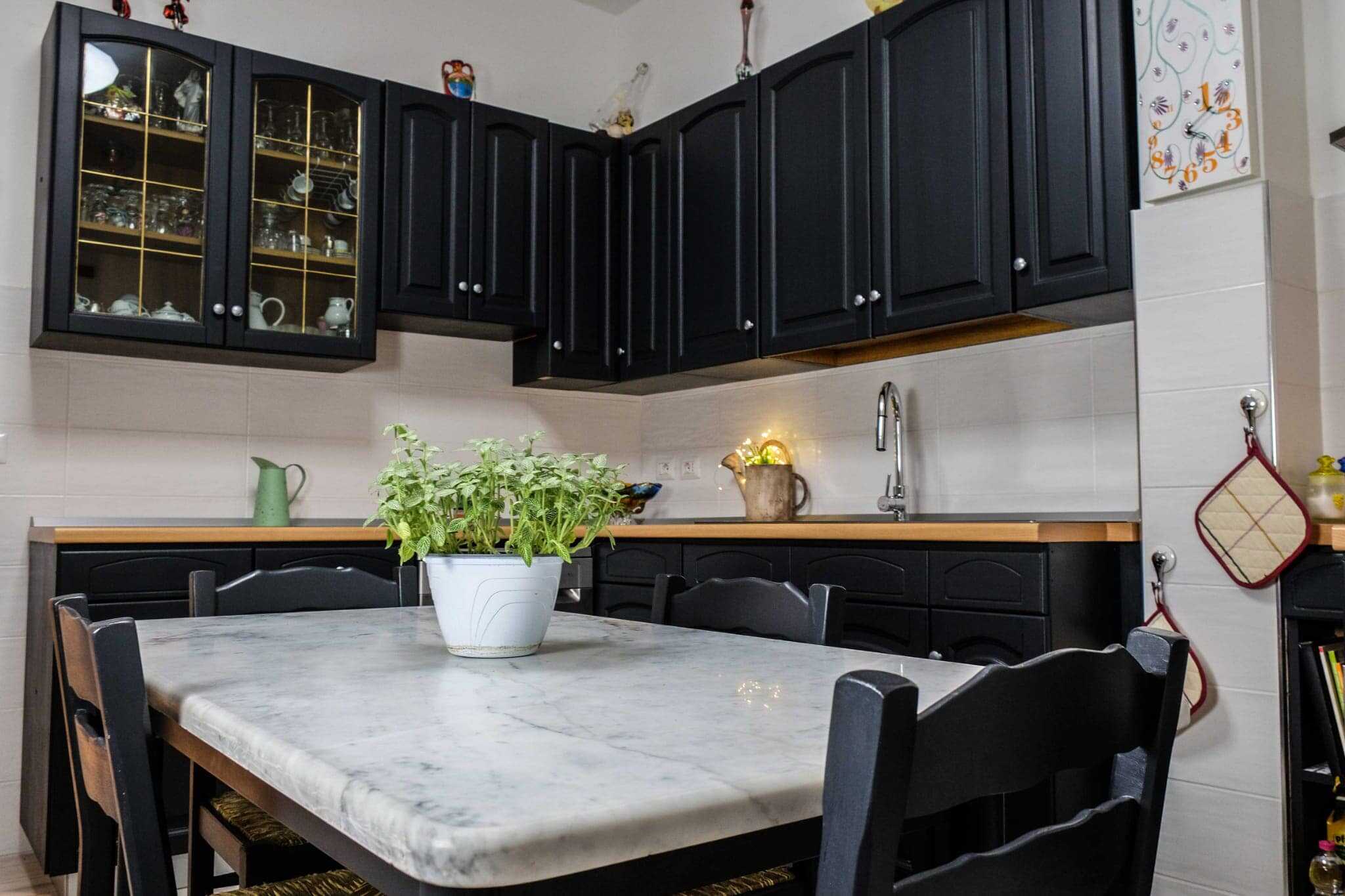 prima-dopo-cucina-legno-nero Lavagna di cucina moderna con ante nere e tavolo in marmo bianco, ambiente elegante e funzionale.